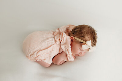 newborn baby girl curled on beanbag laying on her belly with hands and feet tucked under her photo captured by lubbock newborn photographer Mary Wiebe