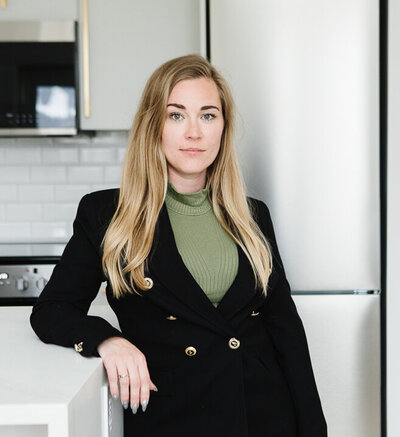 Professional Realtor Tamara Rzan standing beside a kitchen island of a pristine, white home.