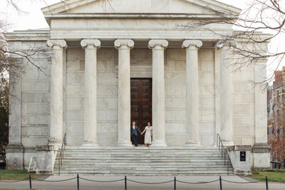 Princeton University | Couple holding hands for pre-wedding photo by columns of campus building | New Jersey