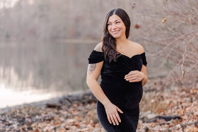 A pregnant woman in a black dress with a lake in the background.
