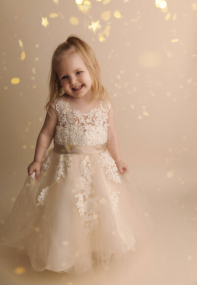 sweet girl wearing tan and white dress in studio tan backdrop with star glitter photo session near bellevue