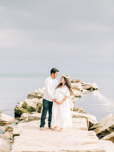 husband and wife holding belly for maternity photos at the beach