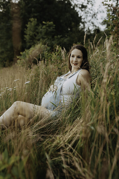 Verona B Photography captures a stunning maternity picture of a mom sitting in the grass and holding her belly at Silver Creek Metro Park in Norton, OH. The mom gazes serenely off into the distance while the sun is setting in this beautiful setting near Akron, OH.