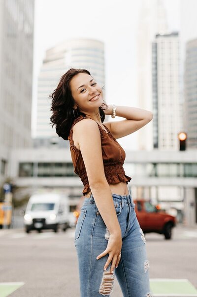Senior girl in a brown top and jeans posing in front of a busy city street