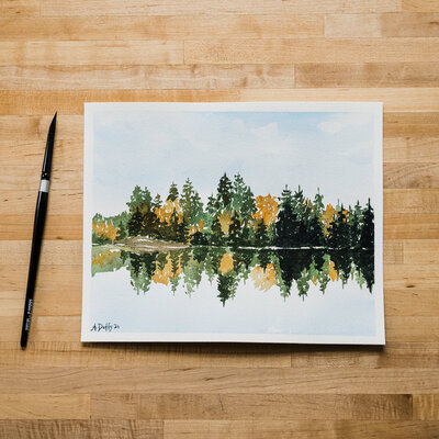 Watercolor painting of an autumn color forest reflecting on a lake in Washington by Amy Duffy