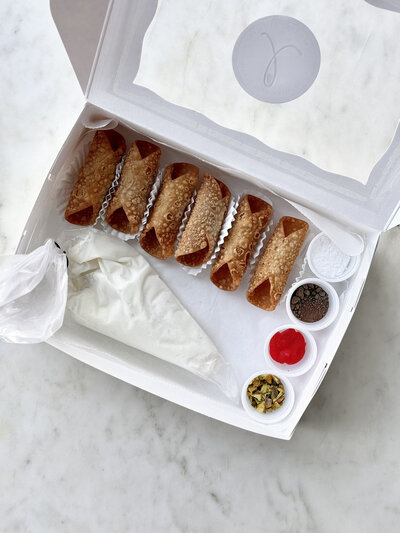 Cannoli shells, ricotta filling, and toppings laid out in a box