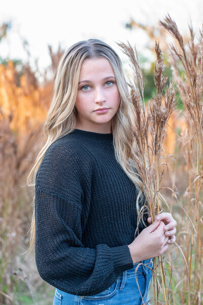 Orlando senior photography at a field in  Baldwin Park photographing a senior girl wearing a black sweater at sunet.
