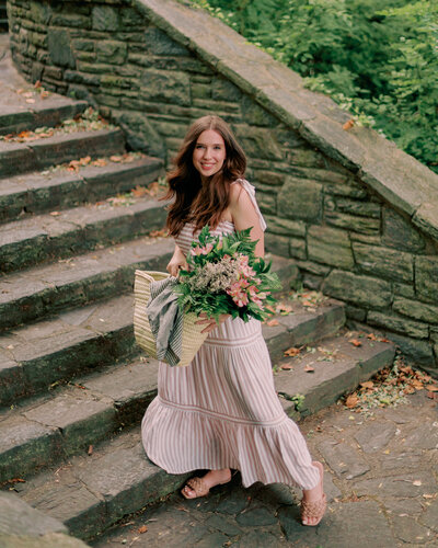 A person in a dress holds florals outdoors on the stairs.