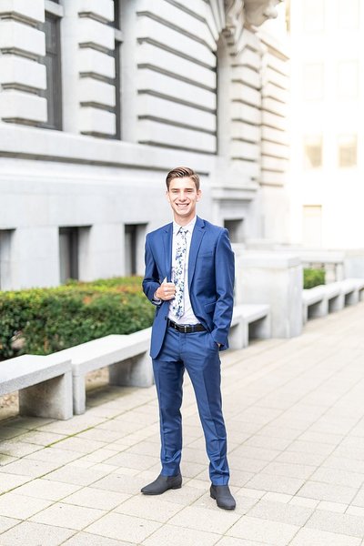 Senior boy wearing cobalt blue suit, white button down, and floral tie in front of courthouse.