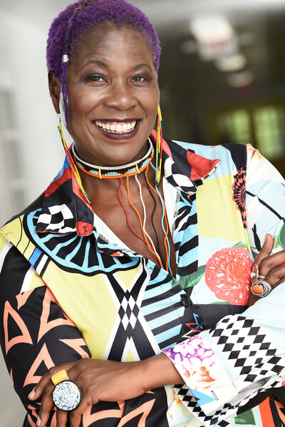 Photo of Lisa Zunzanyika a Black woman with purple hair and a colorful abstract print dress
