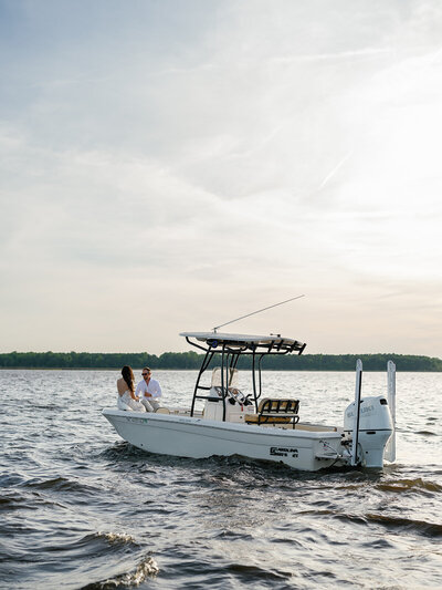 A couple seated on a boat on a lake, sharing a serene moment under the setting sun.