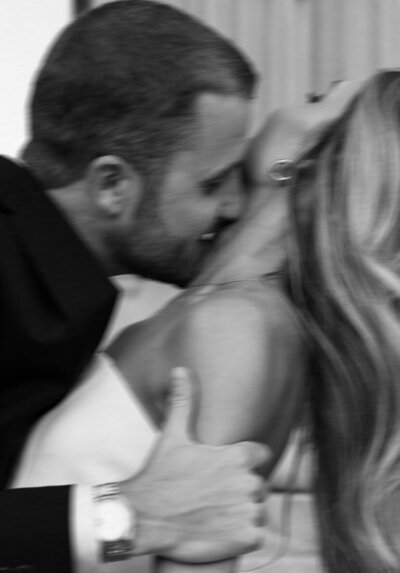A happy image of a groom kissing his bride's neck in black and white