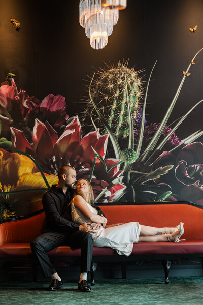 A future bride reclines into her fiancé for a dramatic, moody engagement photo at Hotel Deco in Omaha with Claire Katan.