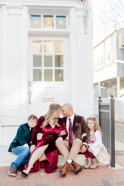 A family of four in christmas colors sit on a stoop hugging each other