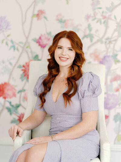 Headshot of Ashley in a purple dress sitting in a white chair