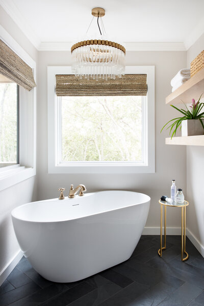 free standing white tub, crystal chandelier, open shelving, bamboo shades in the bathroom