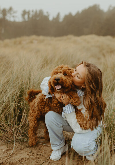 girl kissing fluffy dog in beach grass