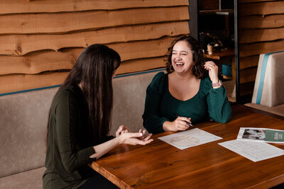 two people laughing with each other while sitting at a table