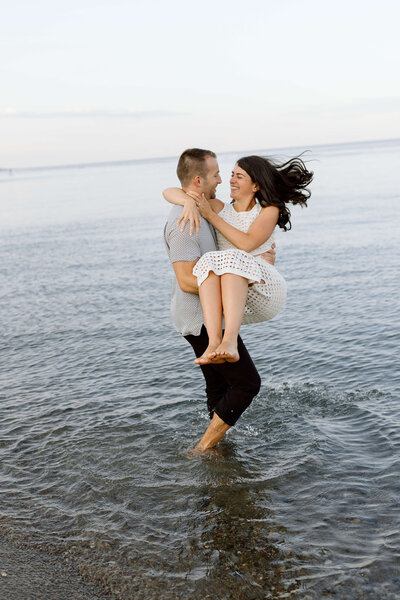 A man lifting his fiance and spinning her around while standing in the water