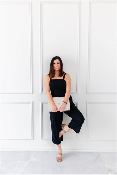 Woman in a black jumpsuit holding a laptop explaining website copywriting packages