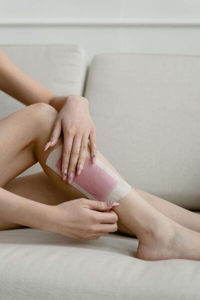 A close-up of a woman's leg being waxed with a pink wax strip, showcasing the professional waxing services available at 212 Salon, Spa, & Barbershop.