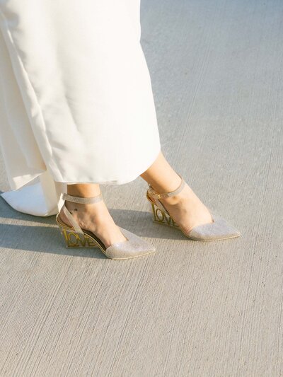 A close up of silver and gold bridal shoes with "love" written in the heel.