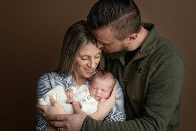 A timeless studio portrait celebrating the love and joy of new parenthood. This image features a newborn safely snuggled in their parents’ arms.
