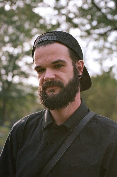 Wedding photographer Drew Anderson smiles while standing in the snow in plaid 