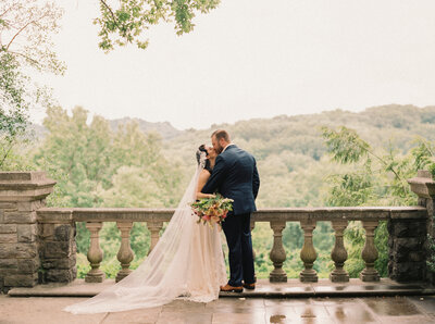 Bride with long lace veil kisses groom over looking the gardens at Cheekwood in Nashville Tennessee photographed by Nashville wedding photographer Magnolia Tree Photo Company