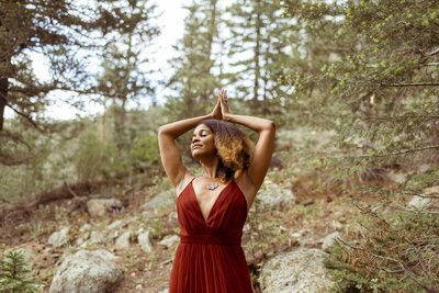 woman with a flower crown and a red dress standing in the forest with palms joined above her head