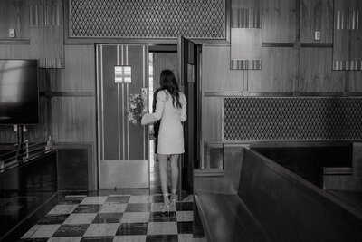 Black and white photo from behind of bride in a short dress walking through a courthouse door