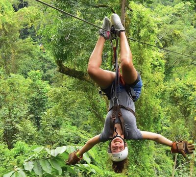Me ziplining upside down in front of a lush green jungle in Costa irca