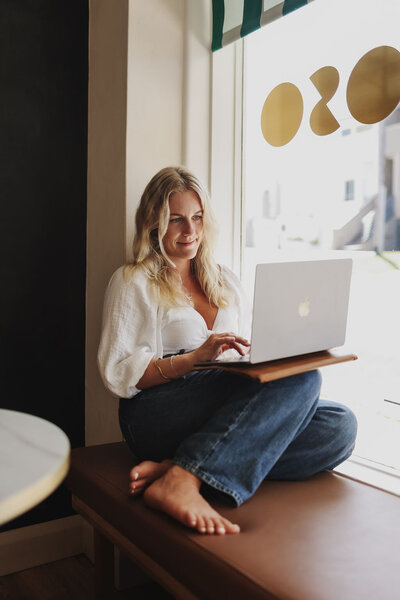 Woman sitting in window of a cafe, working on her laptop