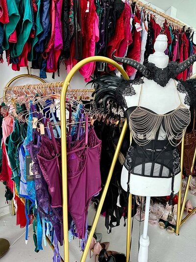 Mannequin displaying elegantly styled top with large selection of clothing in background.