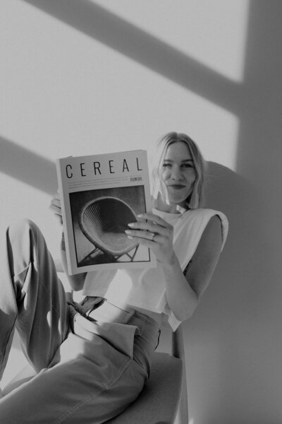 Delcy Garnaas sits in chair with cereal magazine looking towards camera