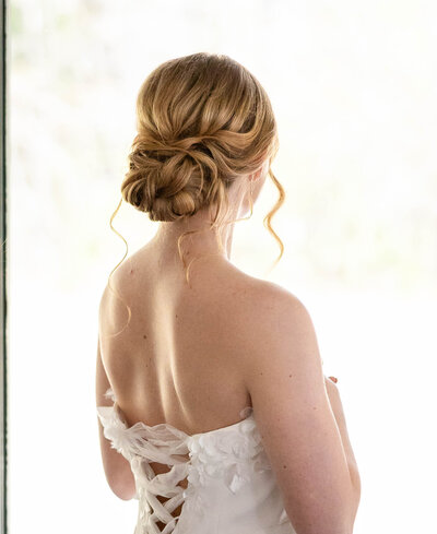 The back of a bride with an updo chignon hairstyle of strawberry blonde color.  Back of wedding gown that is laced up in the middle