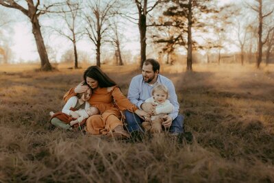 During an at home Warner Robins lifestyle family photo session, a woman playfully puts a pot on a man's head and holds a wooden spoon while he sits with a baby in a high chair at the dining table.