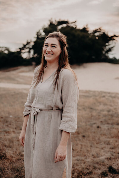 Lianne van der Kwast. Trouwfotograaf - bruidsfotograaf uit Apeldoorn, Veluwe, Gelderland. De foto is genomen tijdens het golden hour, Lianne lacht en draagt een zandkleurige jurk. Lianne houdt van de natuur, is een bakfietsmoeder, interiorjunkie en heeft een zwak voor liefdesverhalen.