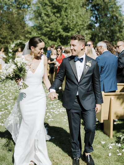 Bride and Groom walking down aisle with white flowers and white dress in outdoor wedding ceremony