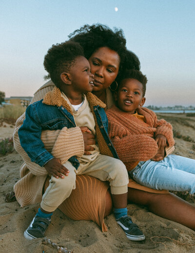 black mom with two sons sitting on the beach at blue hour