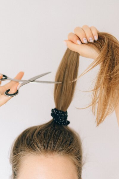 Showit web designer holding scissors near top of ponytail to cut hair