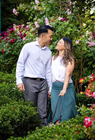 A couple sharing a loving gaze in front of vibrant blooming roses during their couples session – ellobelle photography.
