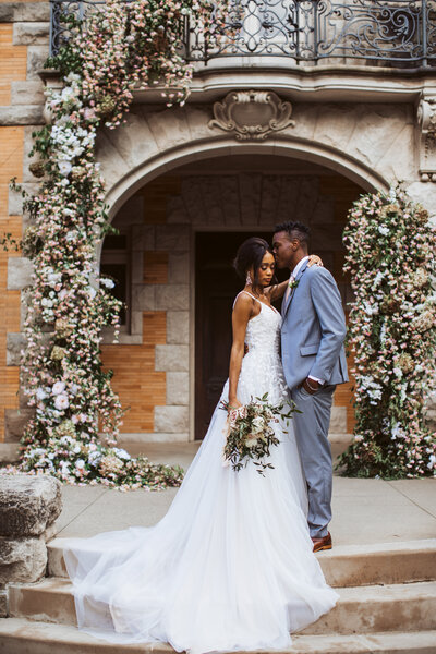 Bride and groom standing in front of a stone venue decorated with floral arches during their Maine wedding.