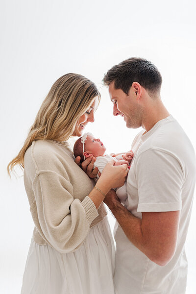 mom and dad smiling with newborn baby girl in studio photography