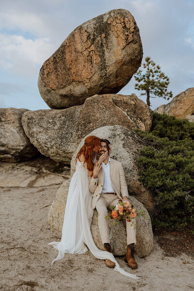 bride and groom sitting on rocks bride kissing grooms cheek