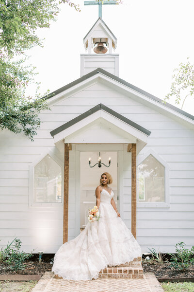 A bride stands in front of the white chapel at The Greenery.
