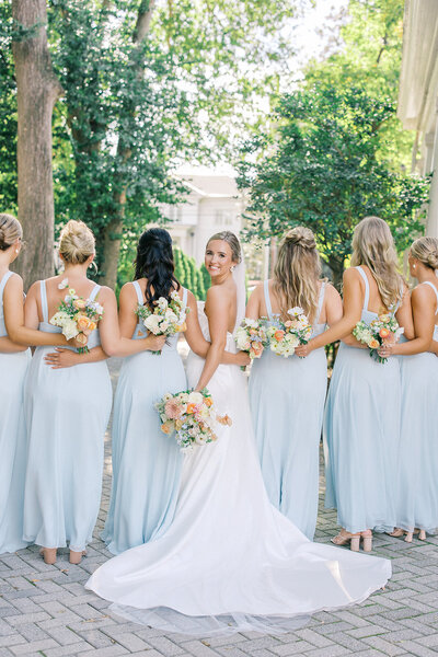 Bride looks back holding bouquet next to bridesmaids in light blue dresses at 255 Milledge wedding in Athens Georgia