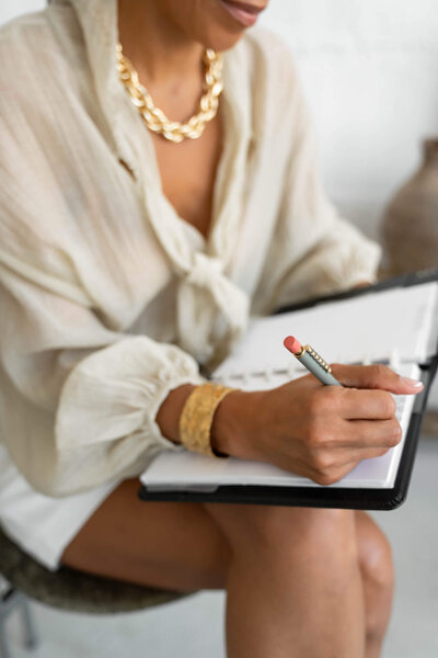  A woman sitting comfortably in a chair, jotting down meeting notes in her agenda.