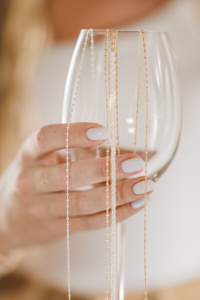 Hand holding a glass with gold and silver permanent jewelry chains draped over it.