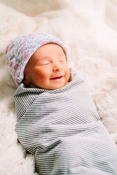 A newborn swaddled in striped fabric, wearing a floral hat, sleeps peacefully in Westchester, NY